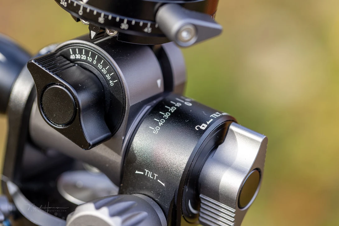 Close-up of a ball head tripod mount with pan and tilt controls against a blurred green background.