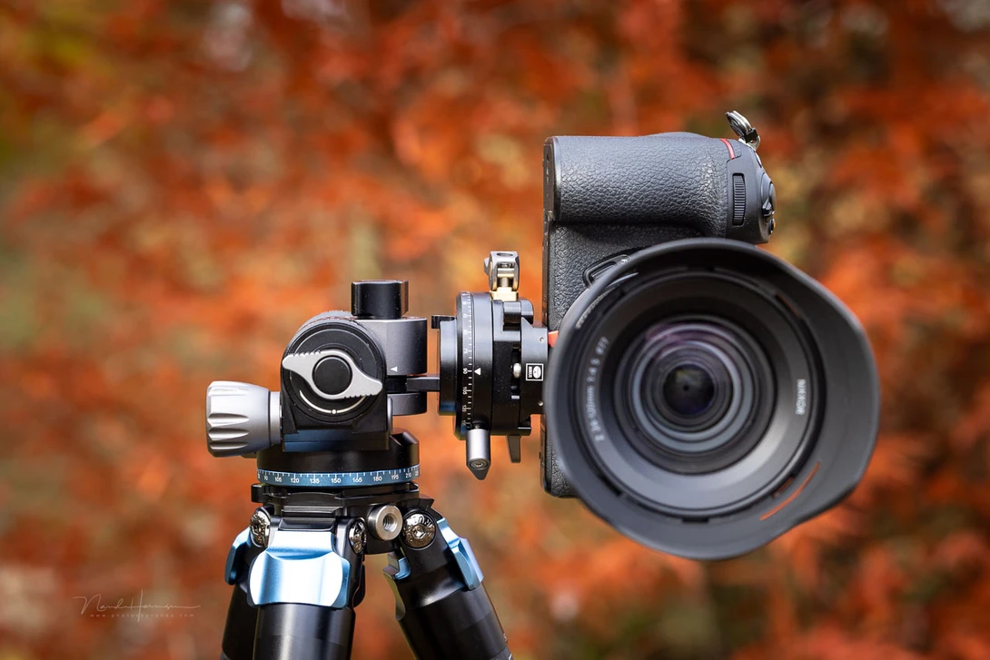 Professional camera lens and tripod head mounted against autumn foliage backdrop.