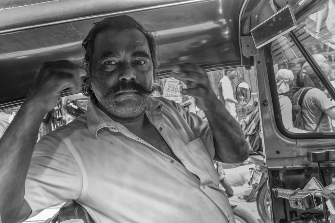 Man with mustache in white shirt inside a vehicle, looking toward camera.