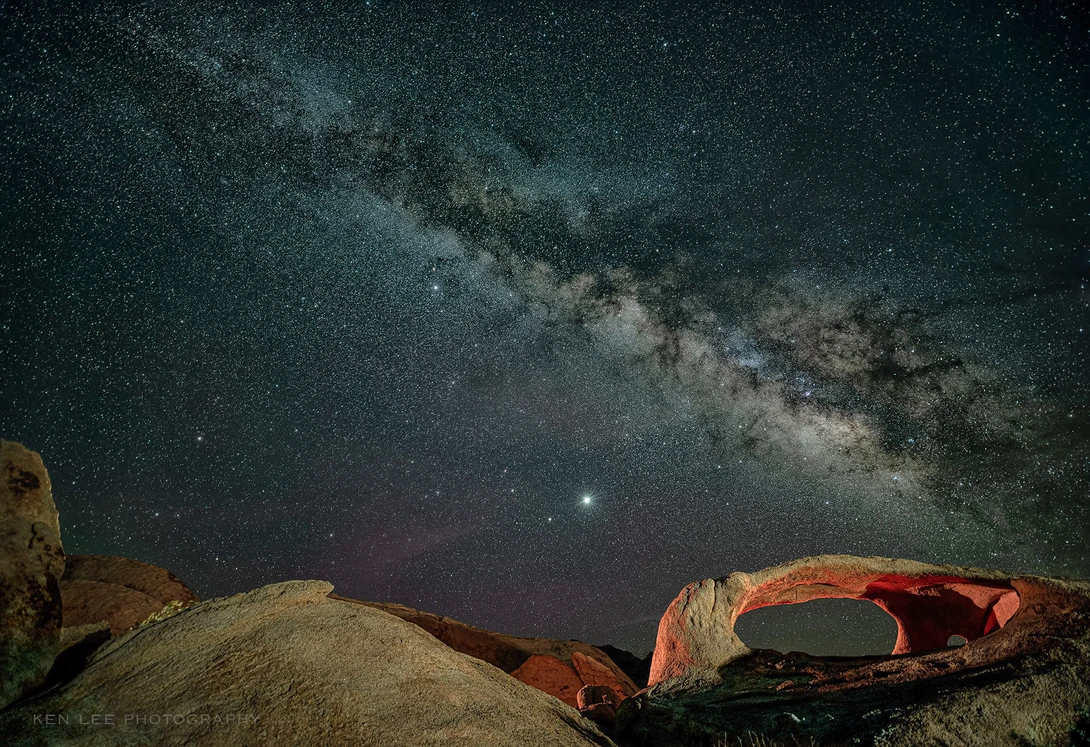Milky Way galaxy arcing over desert rock formations under starry night sky.