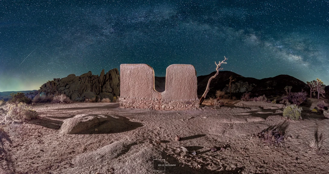 Surreal desert landscape with massive pink U-shaped concrete structure under starry night sky.