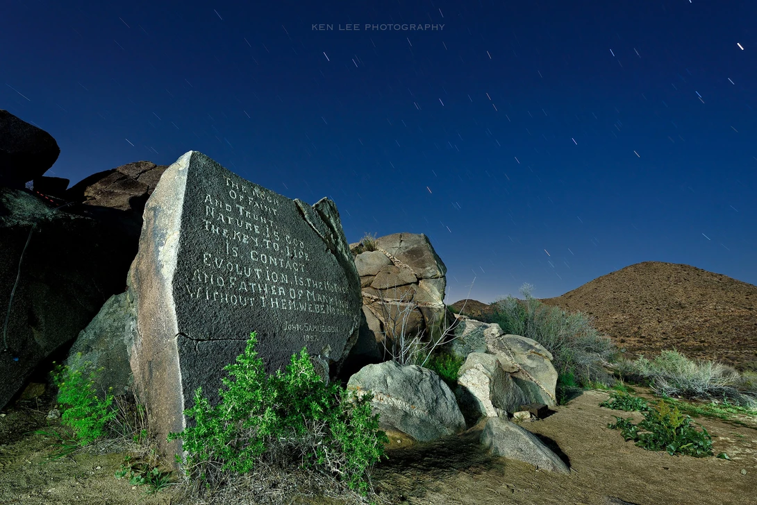 Engraved stone memorial marker among desert rocks under a starry night sky.