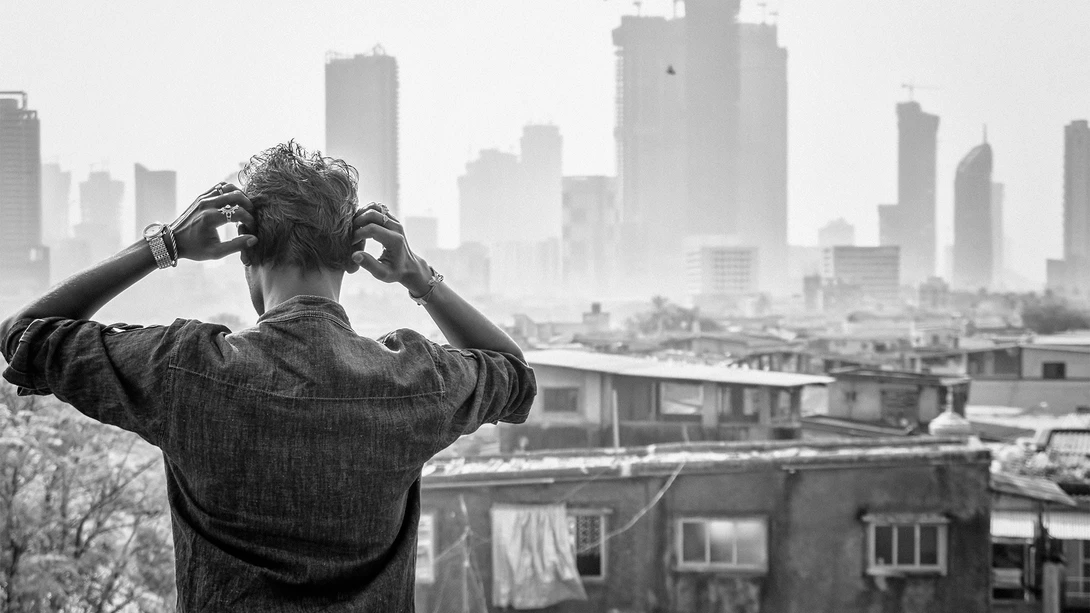Person photographing a city skyline from a rooftop, hands framing the view through a heart shape.