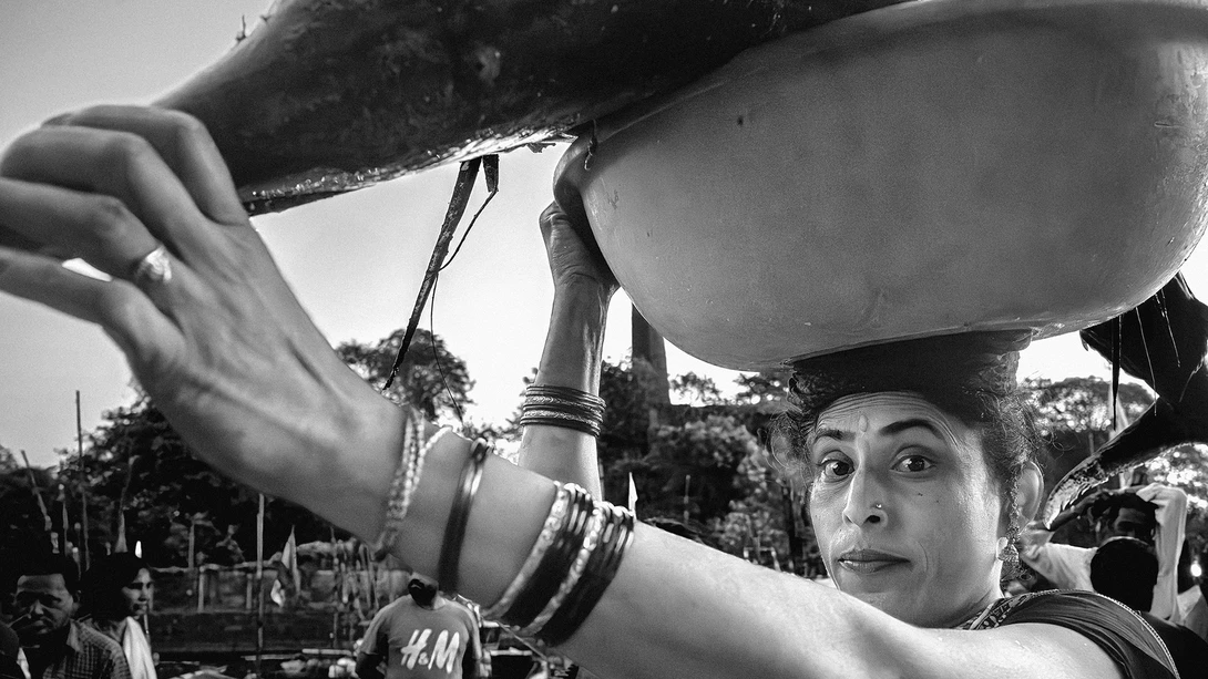 Woman holding large ceramic bowls overhead with expressive face in black and white photograph.