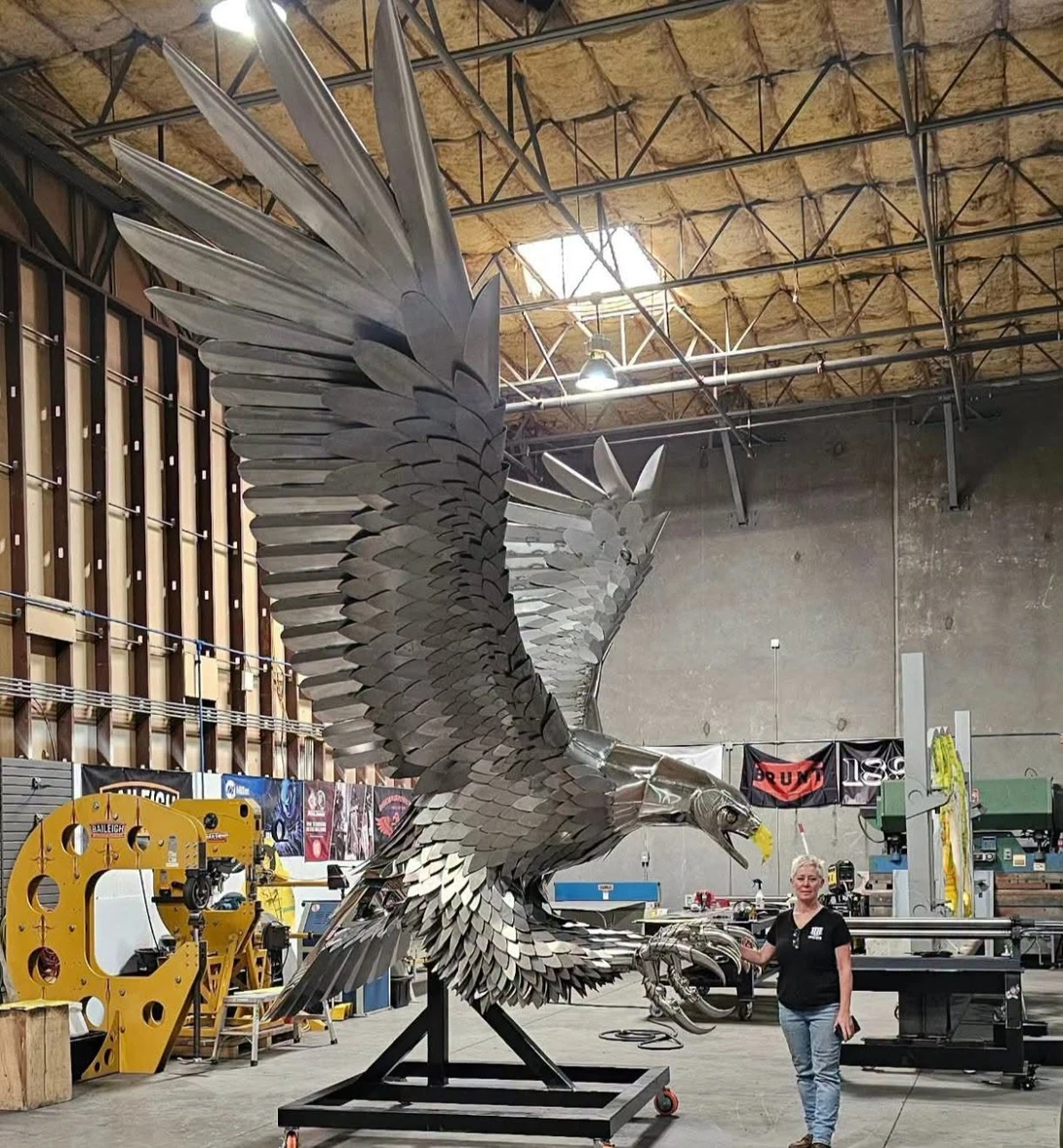 Large metal eagle sculpture mounted on black platform in industrial warehouse space