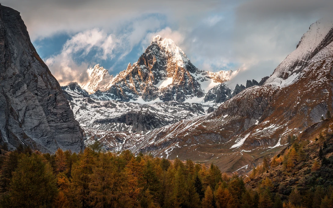 Snow-capped alpine peak framed by golden larch forests and rocky mountain ridges